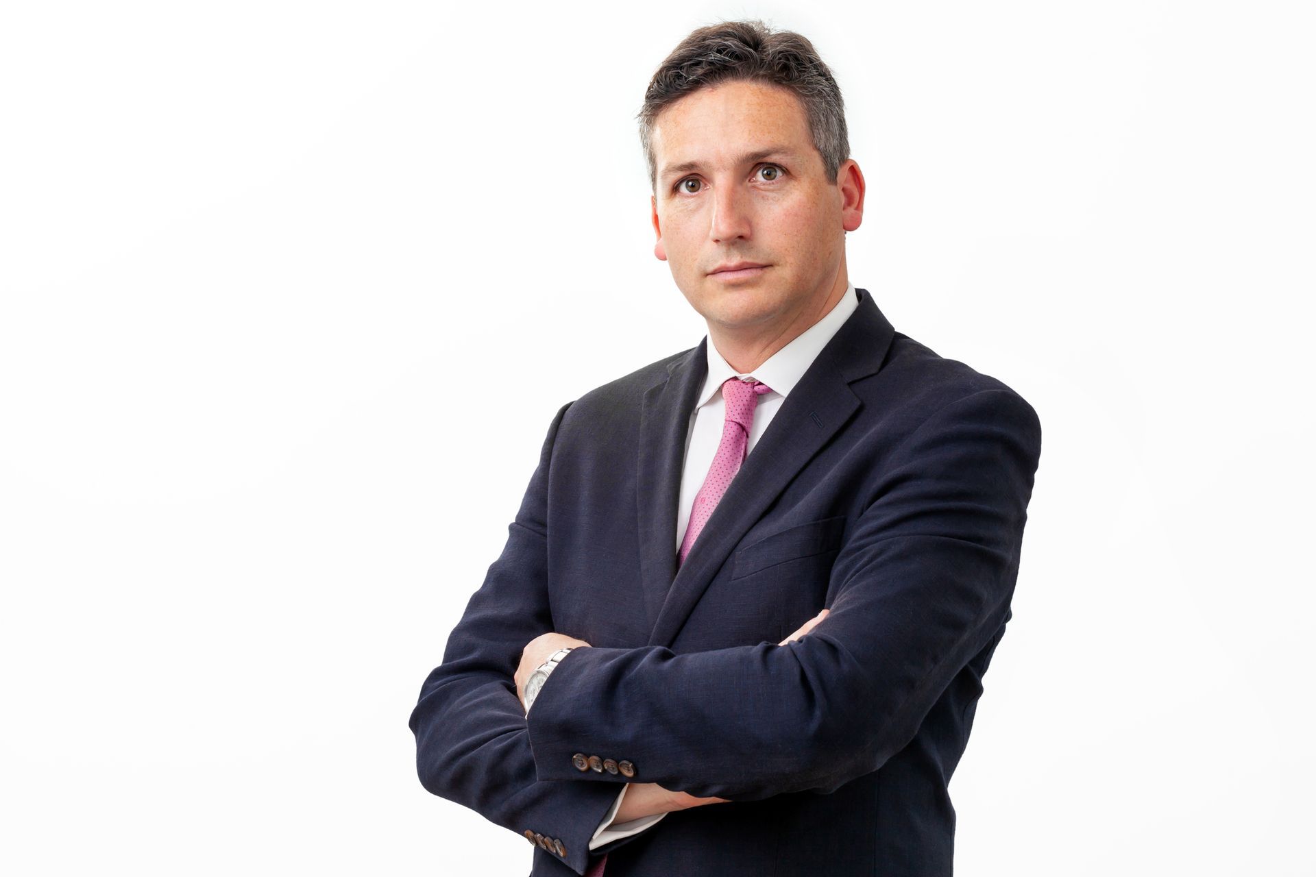 Hombre de traje con los brazos cruzados, mirando directamente a la cámara.