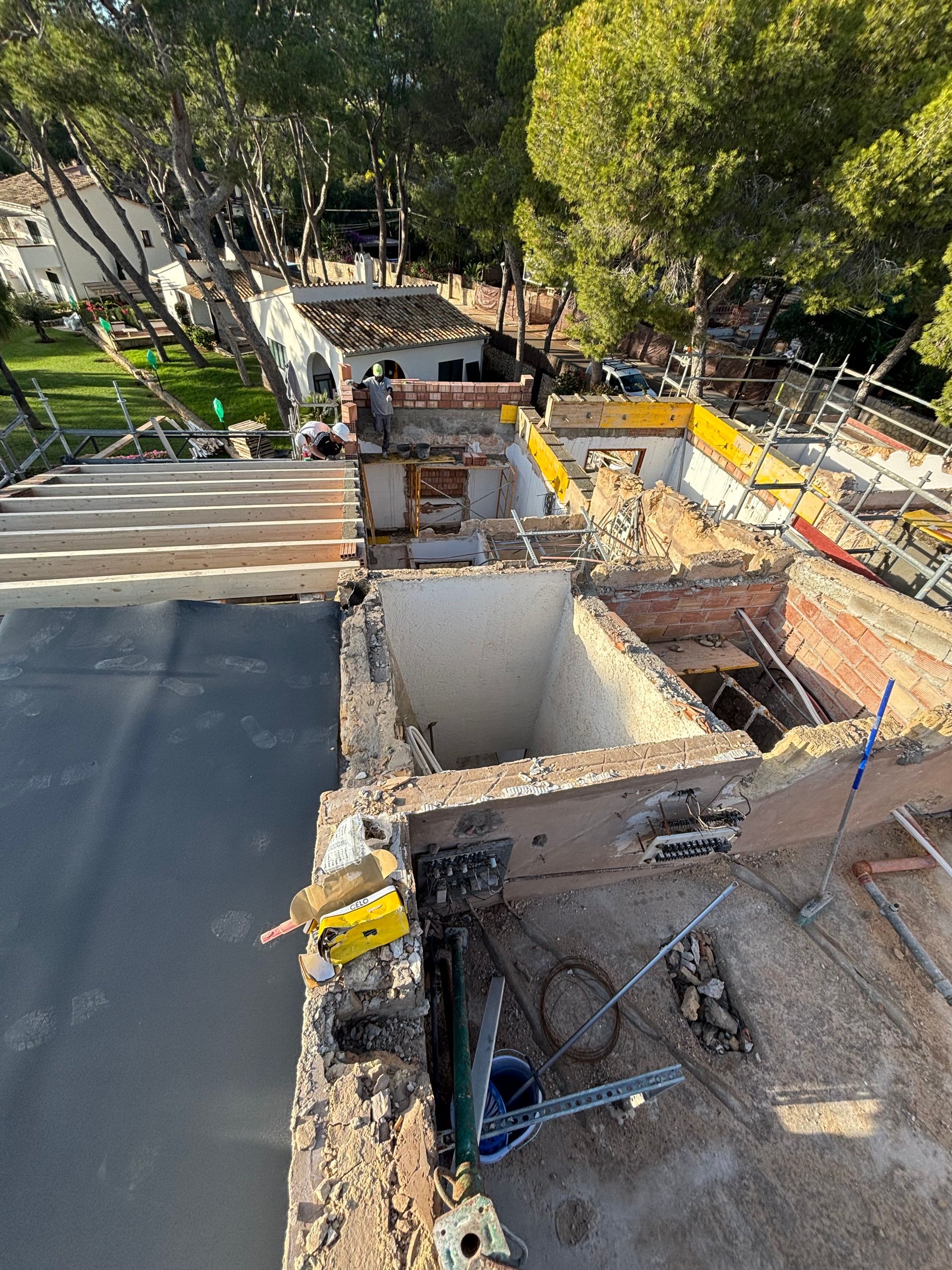 Sitio de construcción desde arriba, paredes de ladrillo a la vista, techo negro, andamios.