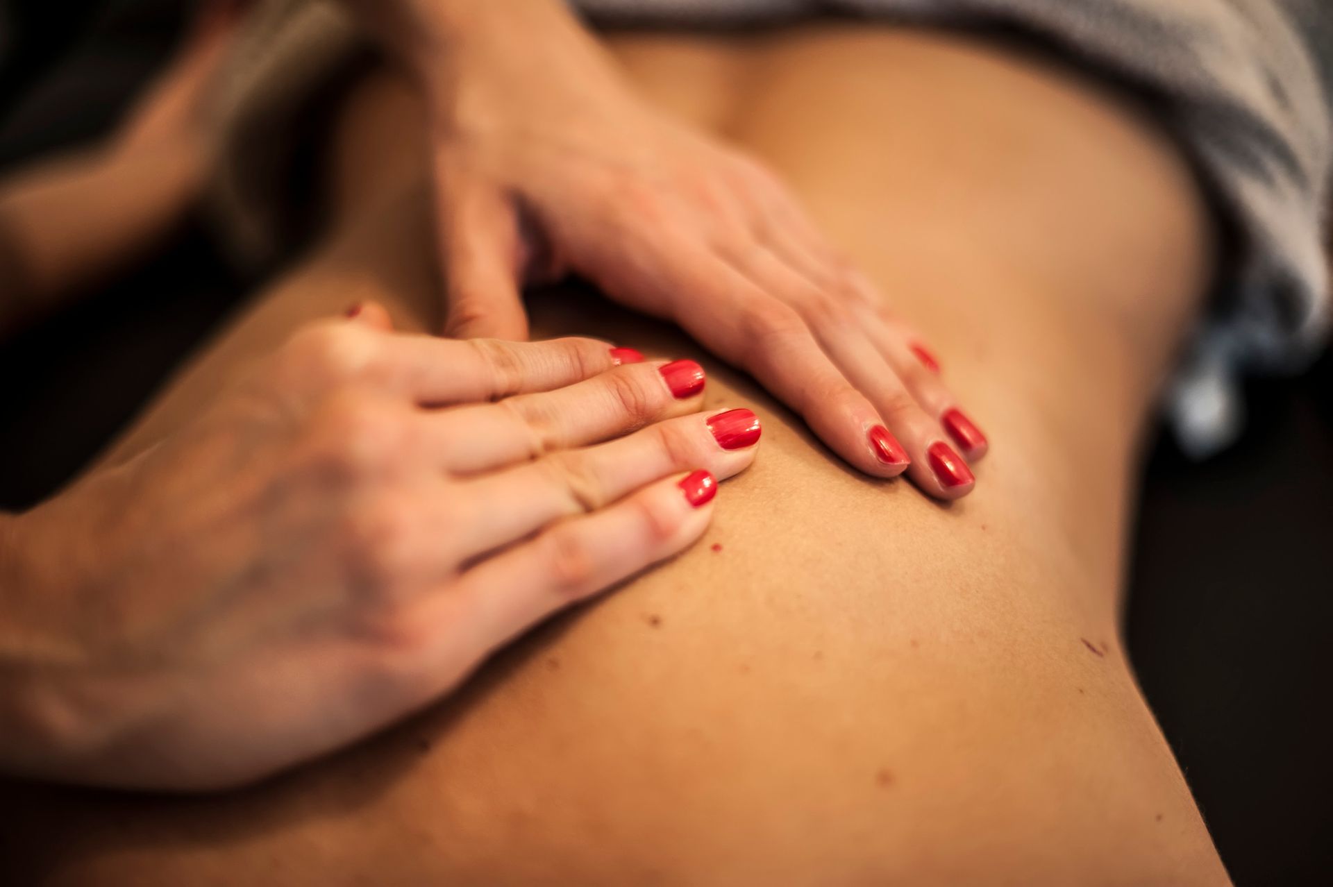 Manos masajeando una espalda desnuda; esmalte de uñas rojo visible.