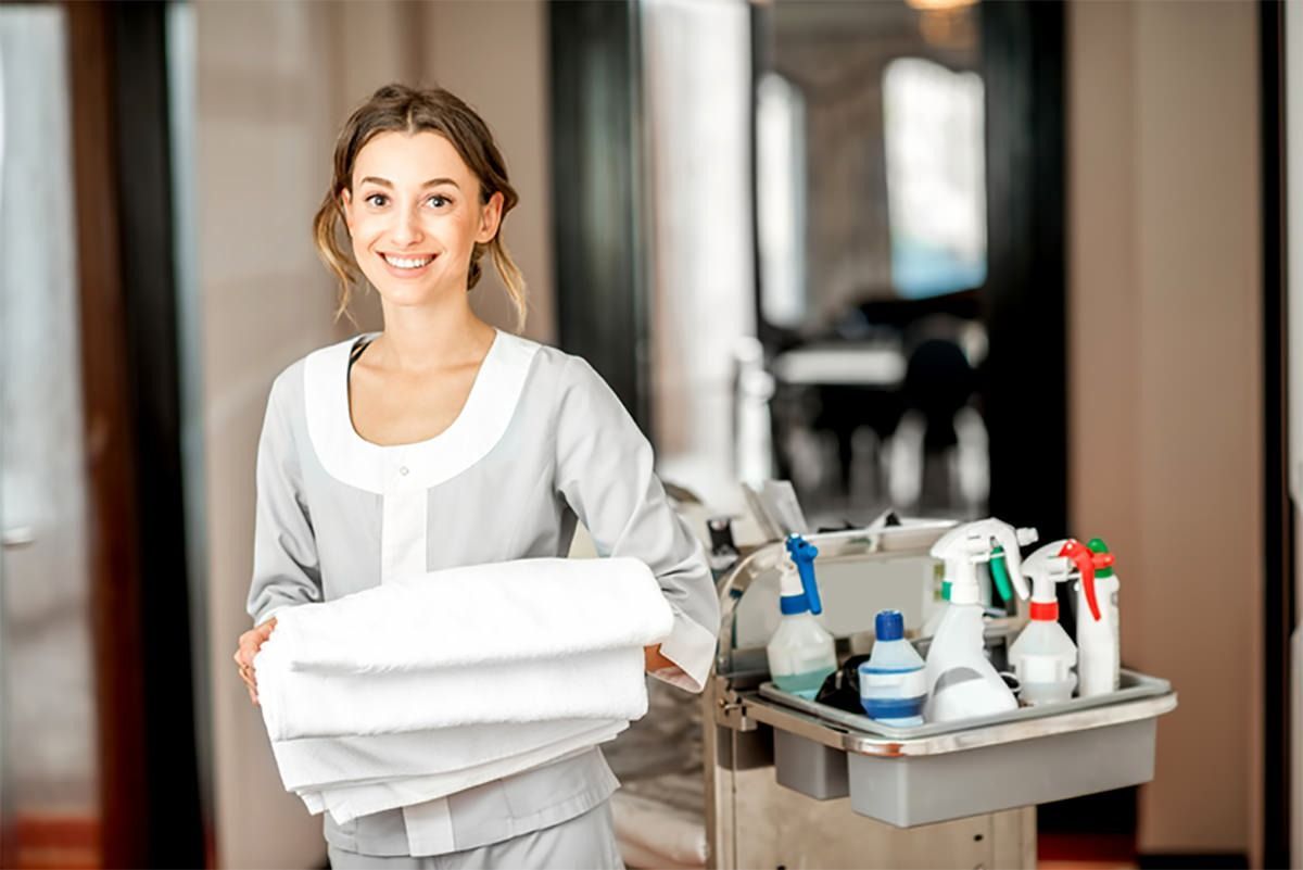 Una criada lleva un carrito lleno de toallas y productos de limpieza.