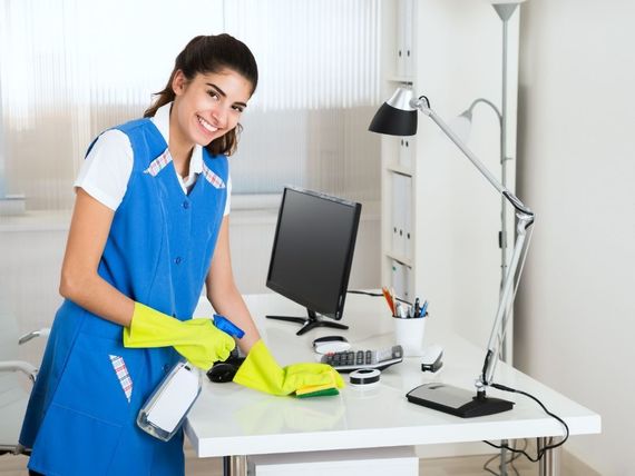Una mujer con un delantal azul está limpiando un escritorio en una oficina.