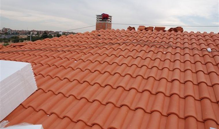 Un techo de tejas rojas con una chimenea al fondo