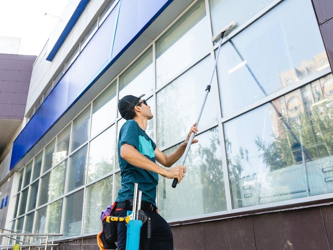 Un hombre está limpiando las ventanas de un edificio con un trapeador.