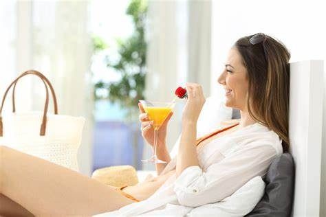 Una mujer está sentada en una cama comiendo una fresa y bebiendo un cóctel.