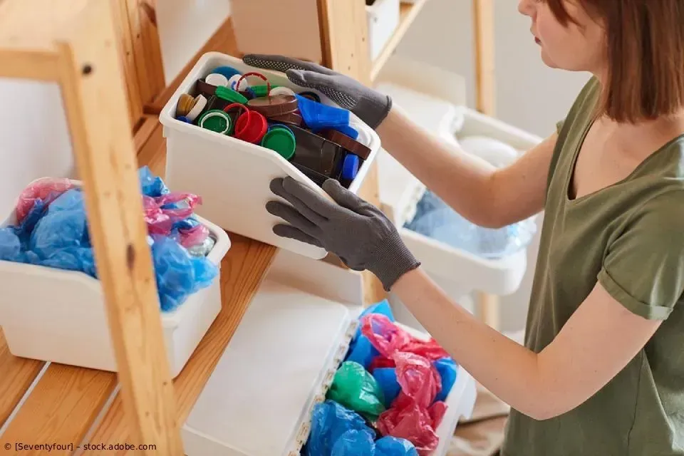 Eine Person mit Handschuhen sortiert bunte Plastikgegenstände in Behälter auf einem Regal in einem Innenraum.