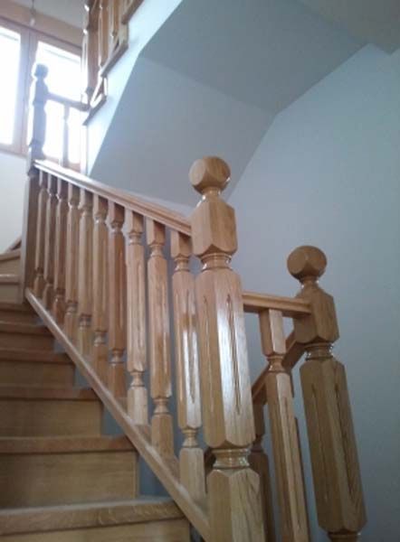 Escalera de madera con barandilla y pasamanos de color claro, que conduce hacia arriba a una ventana.