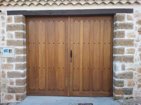 Puertas dobles de madera con tirador oscuro, enmarcadas por columnas de piedra y rematadas por una viga oscura.