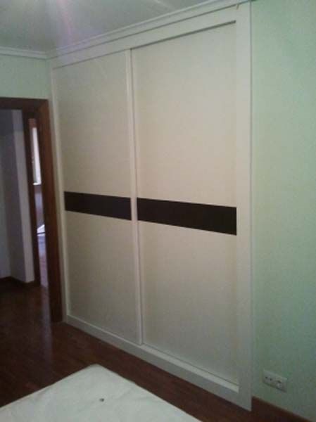 Puertas de armario corredizas blancas con detalles horizontales de color marrón oscuro, colocadas en una habitación.