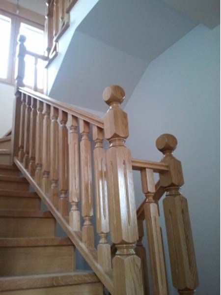 Escalera de madera con balaustrada y pasamanos, ascendente al nivel superior.