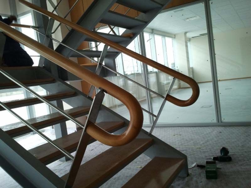 Pasamanos de madera en una escalera metálica. Pared de cristal al fondo.
