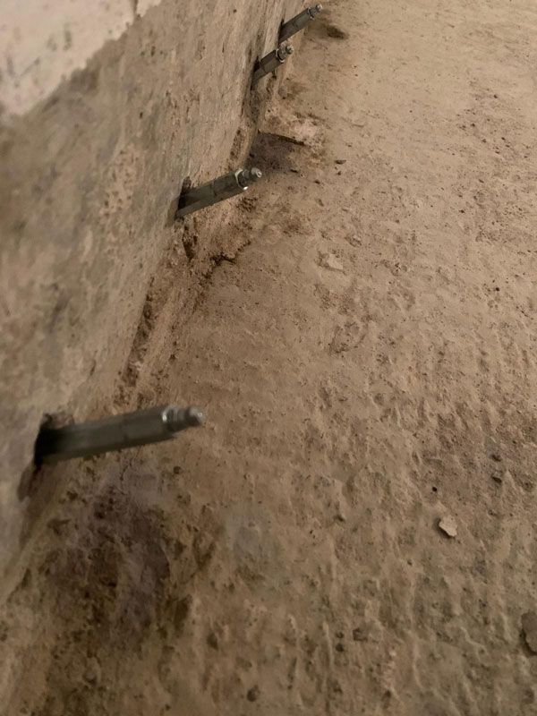 Mehrere Metallstangen ragen aus einer rauen, hellbraunen Wand in Bodennähe heraus.