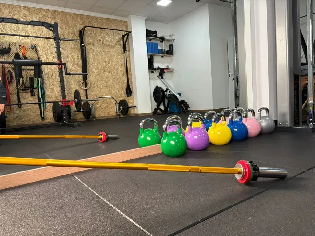 Interior de gimnasio con barras, pesas rusas de colores alineadas y equipos de levantamiento de pesas.