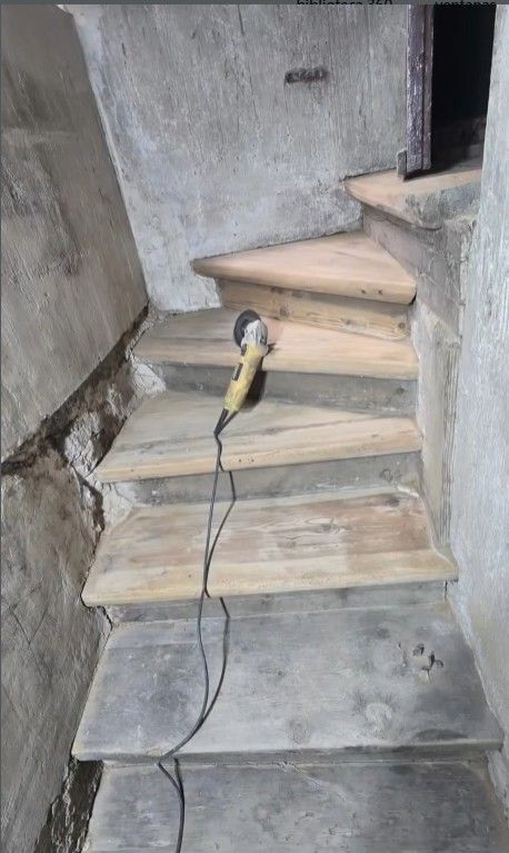 Escaleras de madera con una herramienta eléctrica en un escalón, colocadas en un hueco de escalera de piedra.