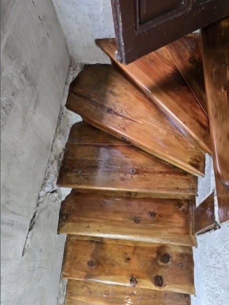 Escalera de caracol de madera en una esquina; los escalones tienen un acabado brillante. Pared de hormigón a la izquierda.