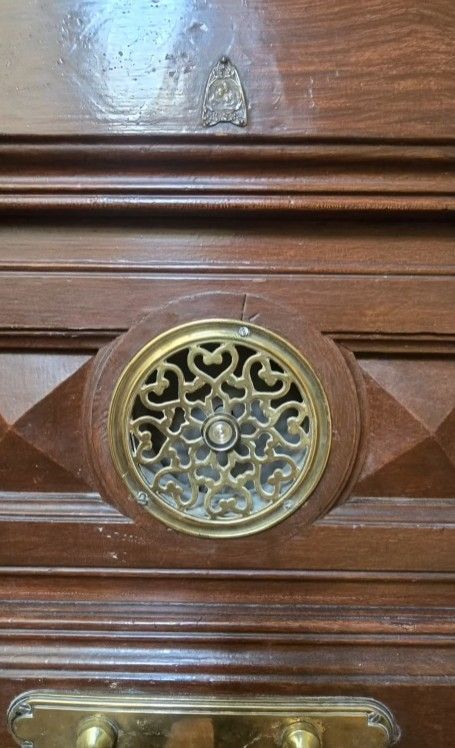 Primer plano de una puerta de madera con ventilación de aire y herrajes de latón decorativos.