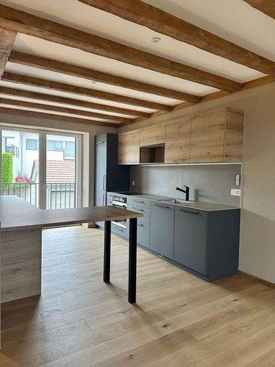 Salon vide et inachevé avec parquet apparent, murs blancs, fenêtres et outils au sol
