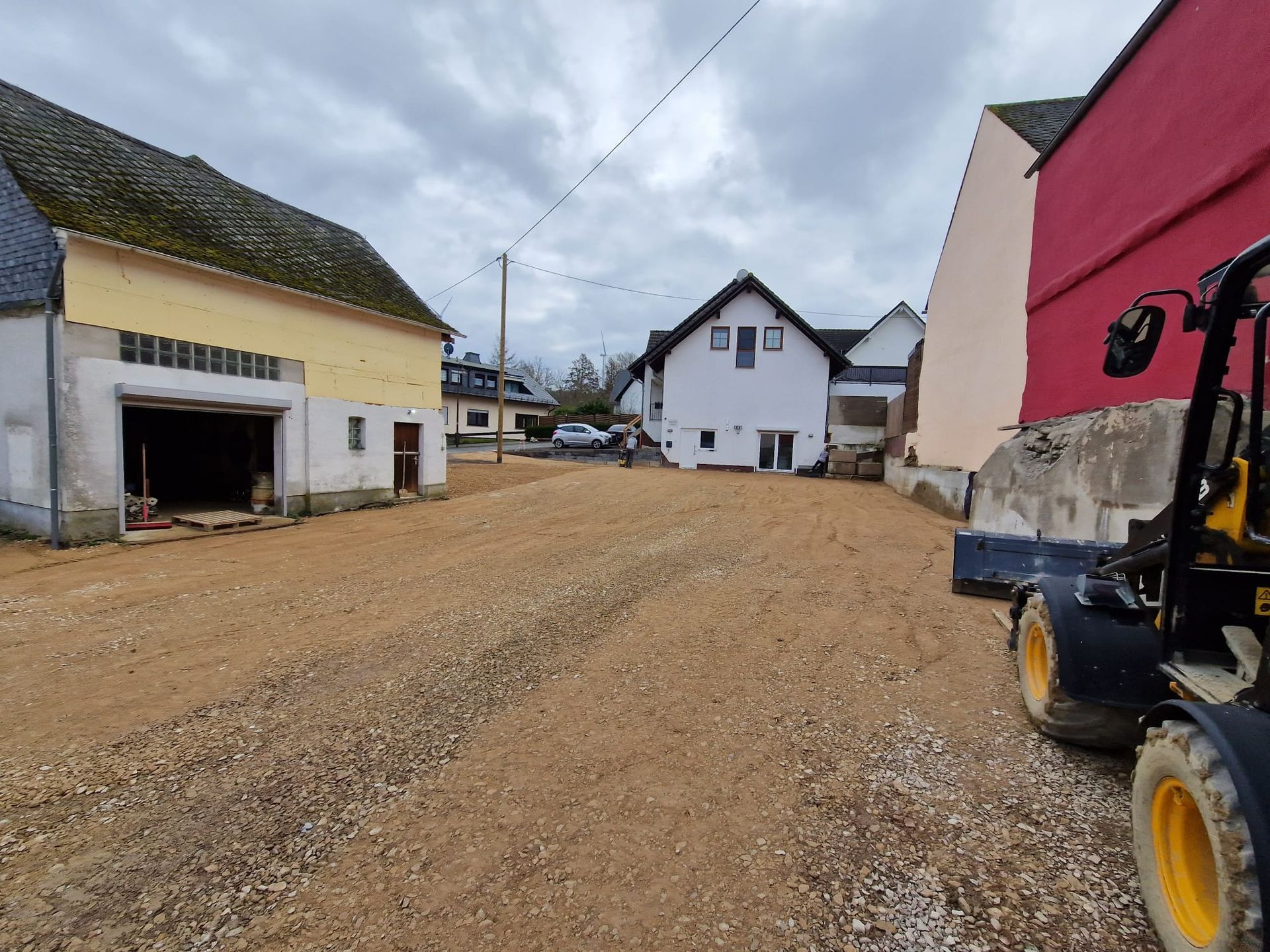 Ein Traktor fährt auf einer unbefestigten Straße zwischen zwei Gebäuden entlang.