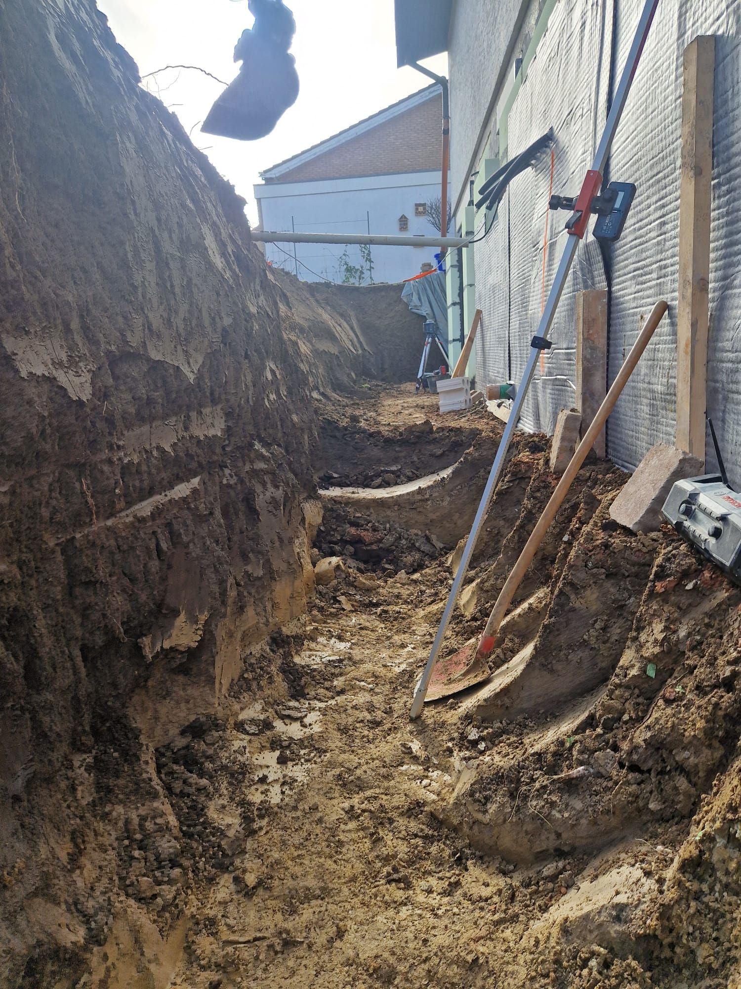 Ein Mann gräbt neben einem Gebäude ein Loch in den Boden.