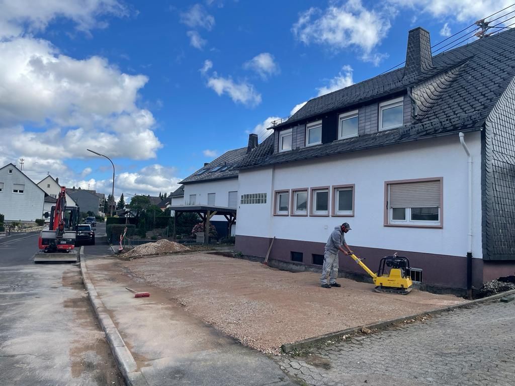 Ein Mann benutzt eine Maschine, um den Boden vor einem Haus zu ebnen.