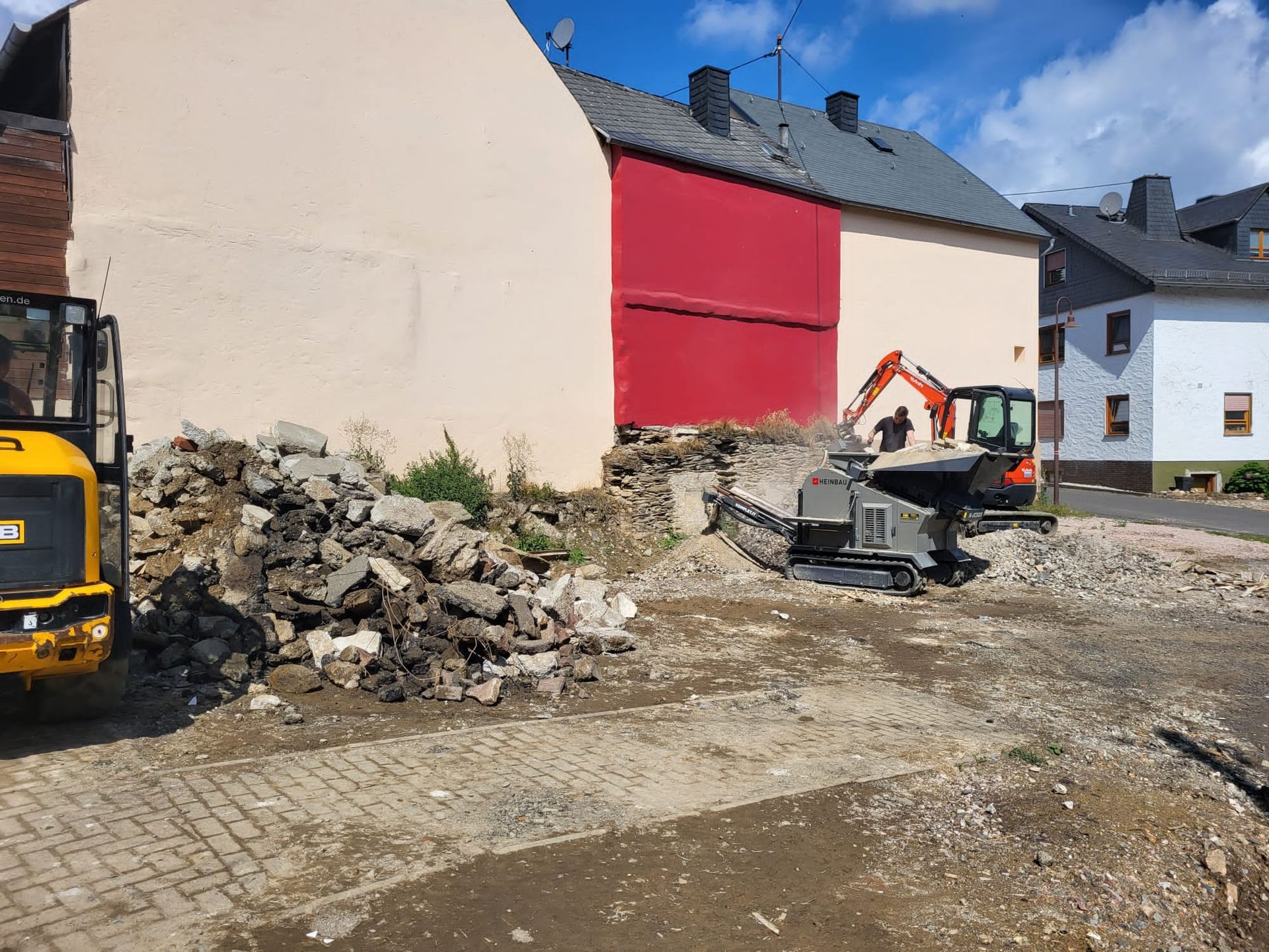 Vor einem Gebäude mit einer roten Tür parkt ein gelber Bagger.