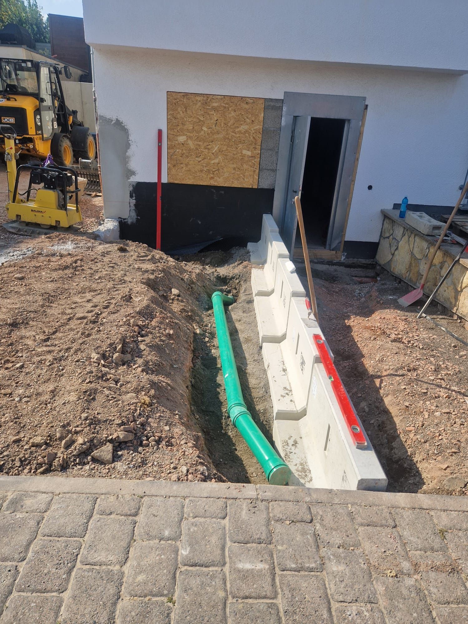 In einem Graben vor einem im Bau befindlichen Gebäude wird ein grünes Rohr verlegt.