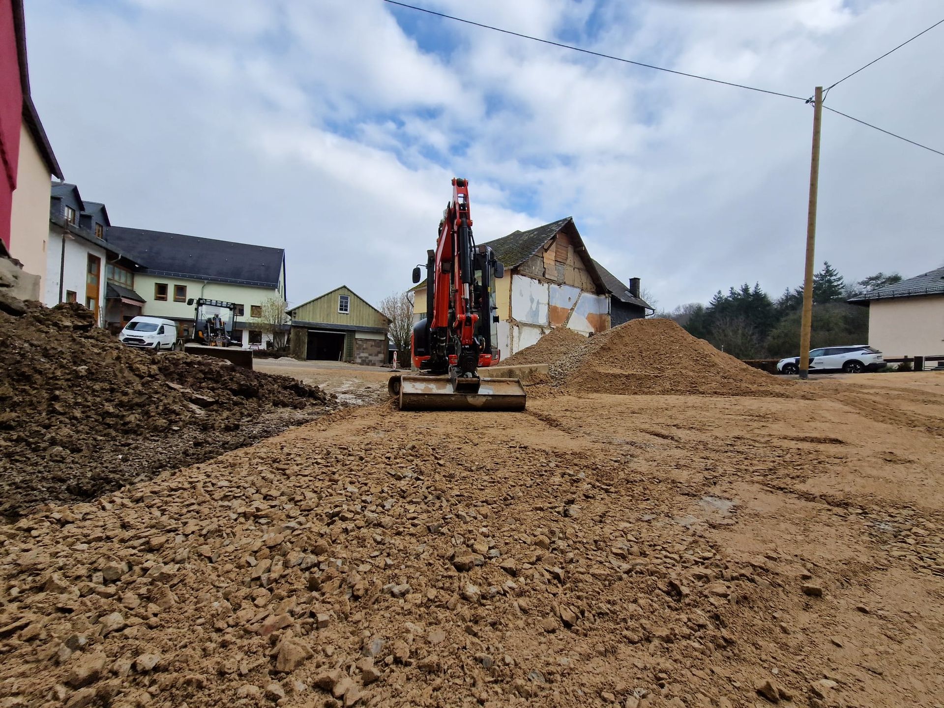 Ein kleiner Bagger steht auf einem Feld vor einem Gebäude.