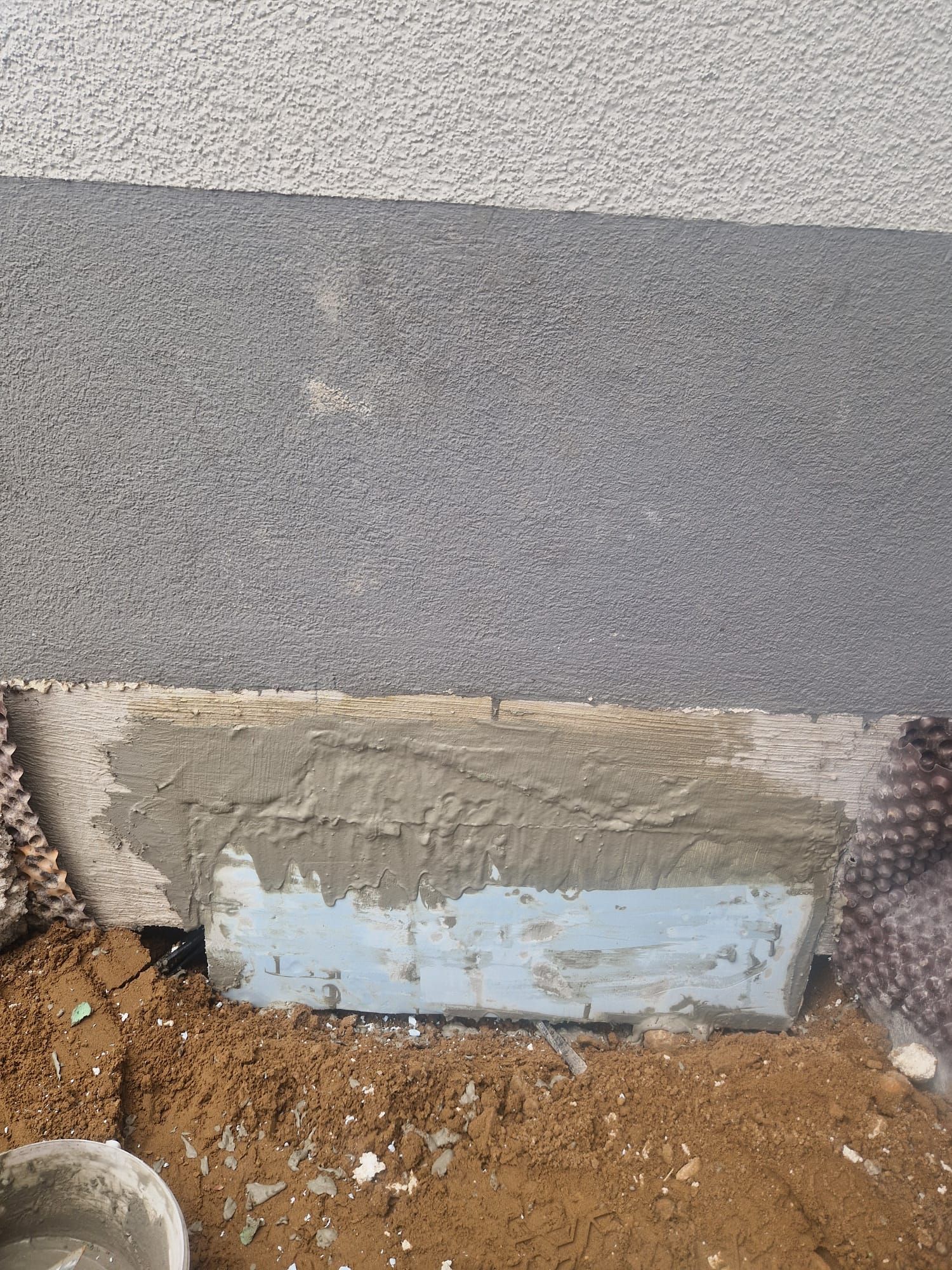 Ein Betonblock liegt auf einem Erdhaufen neben einer Mauer.