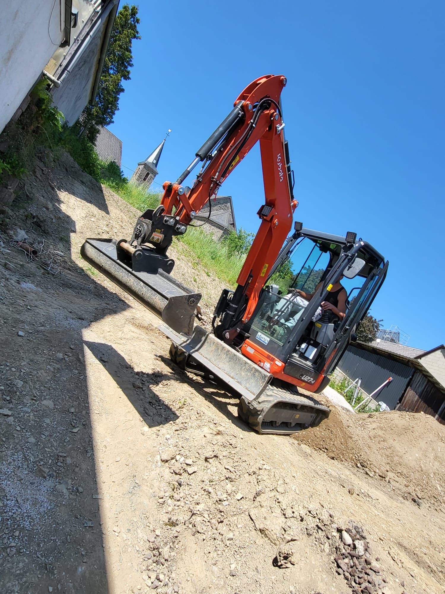 Ein kleiner Bagger fährt einen Feldweg entlang.