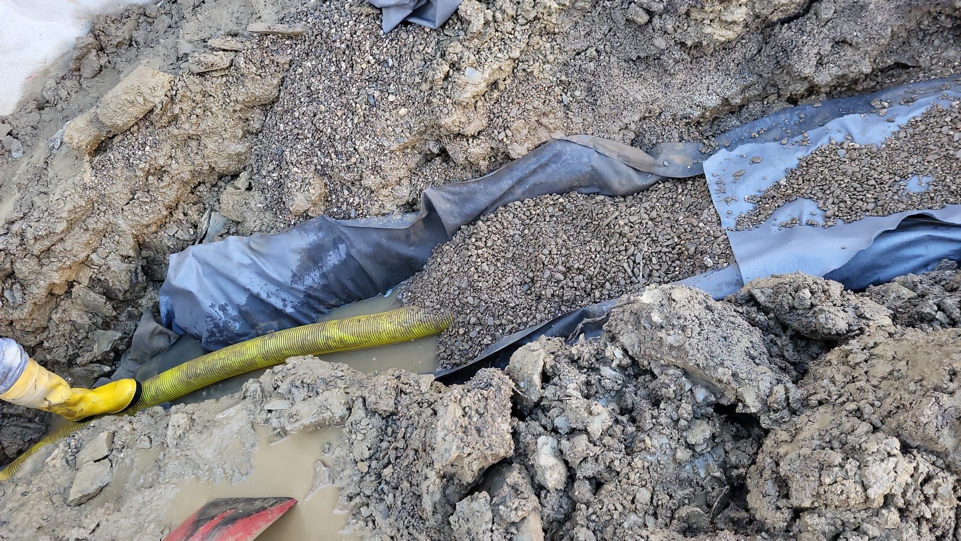 Neben einem Schlauch liegt eine Schaufel im Dreck.