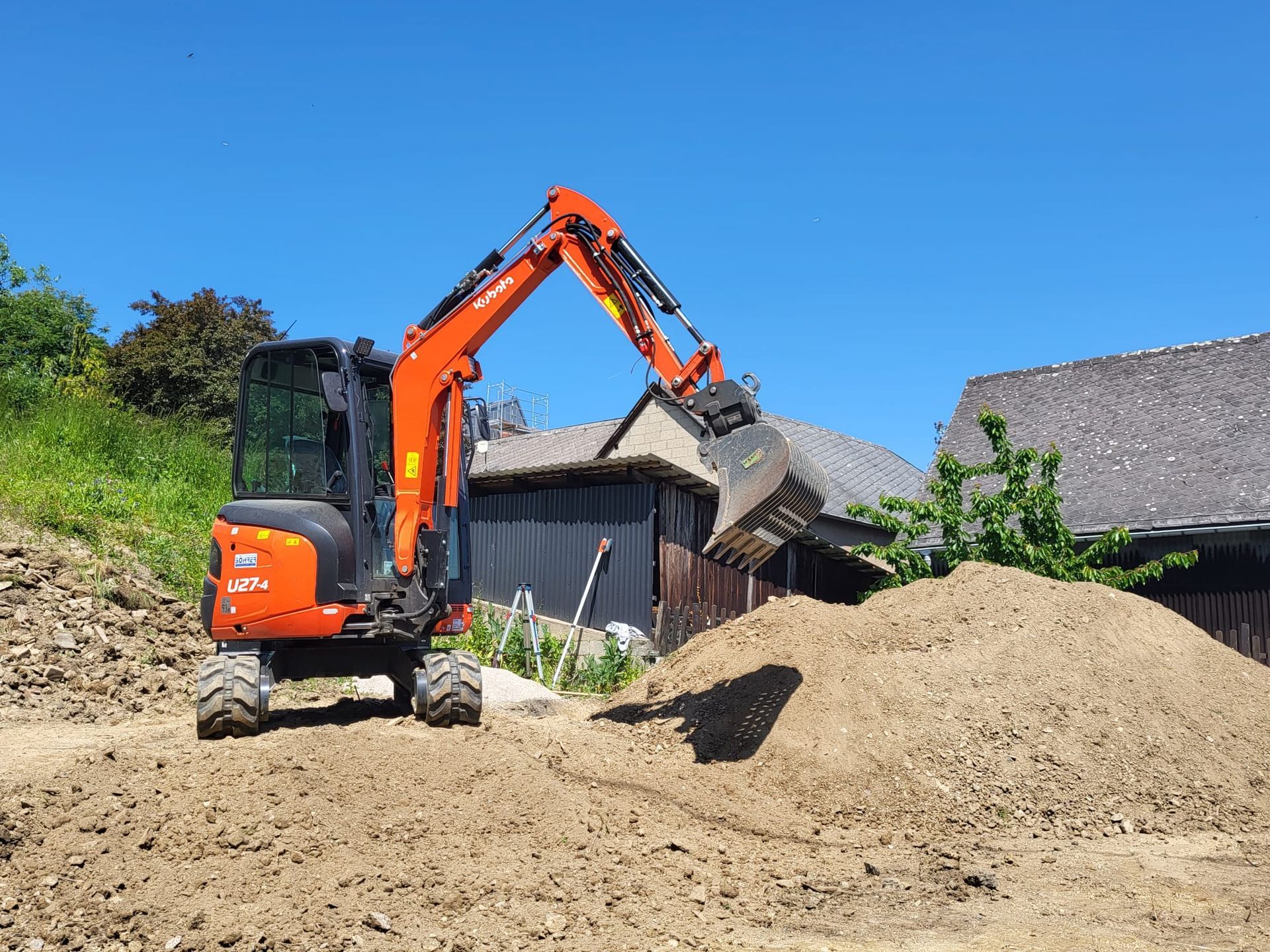 Ein Bagger lädt Erde auf einen Haufen vor einem Haus.