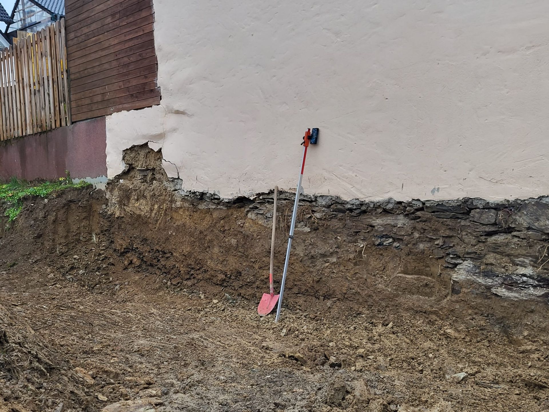 Eine Schaufel liegt im Dreck neben einer Mauer.