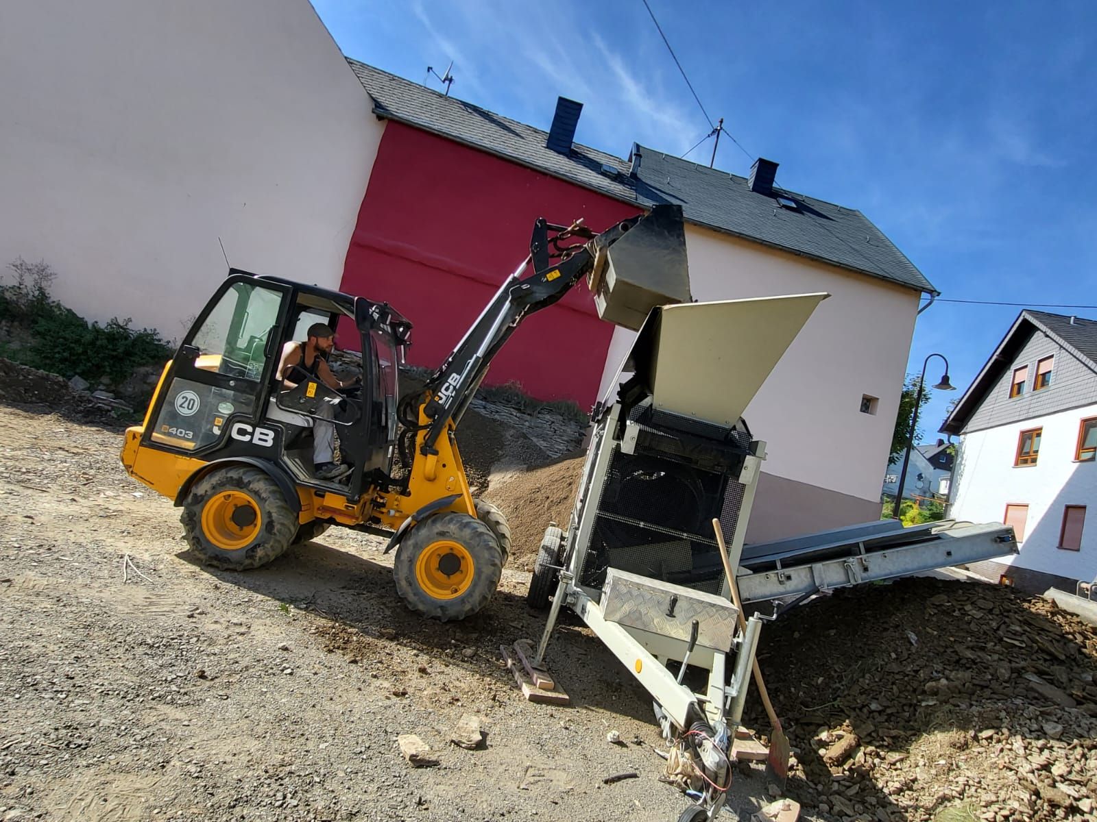 Ein gelb-schwarzer Traktor lädt Erde auf einen Anhänger.