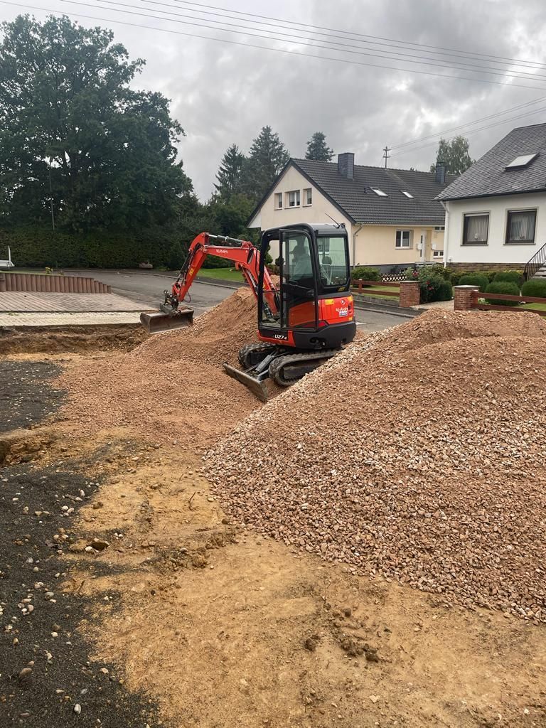 Ein Bagger arbeitet an einem Kieshaufen vor einem Haus.