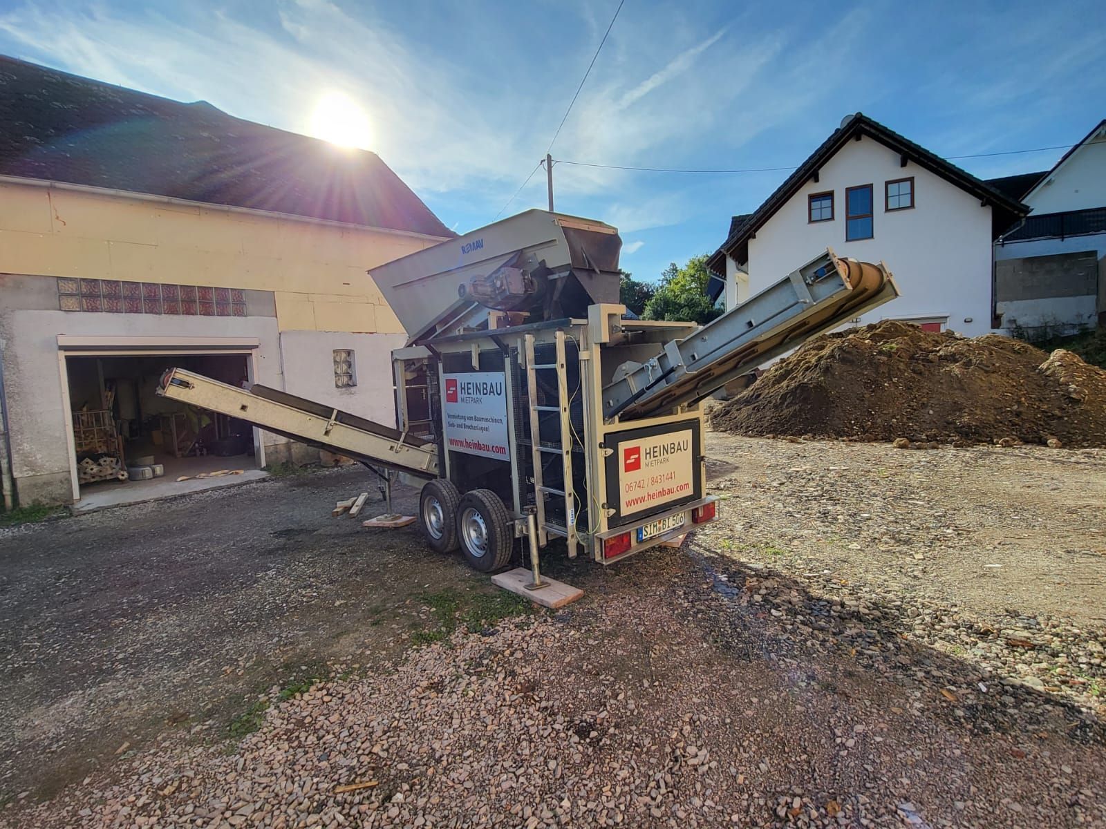 Vor einem Haus steht ein Anhänger mit einem daran befestigten Förderband.