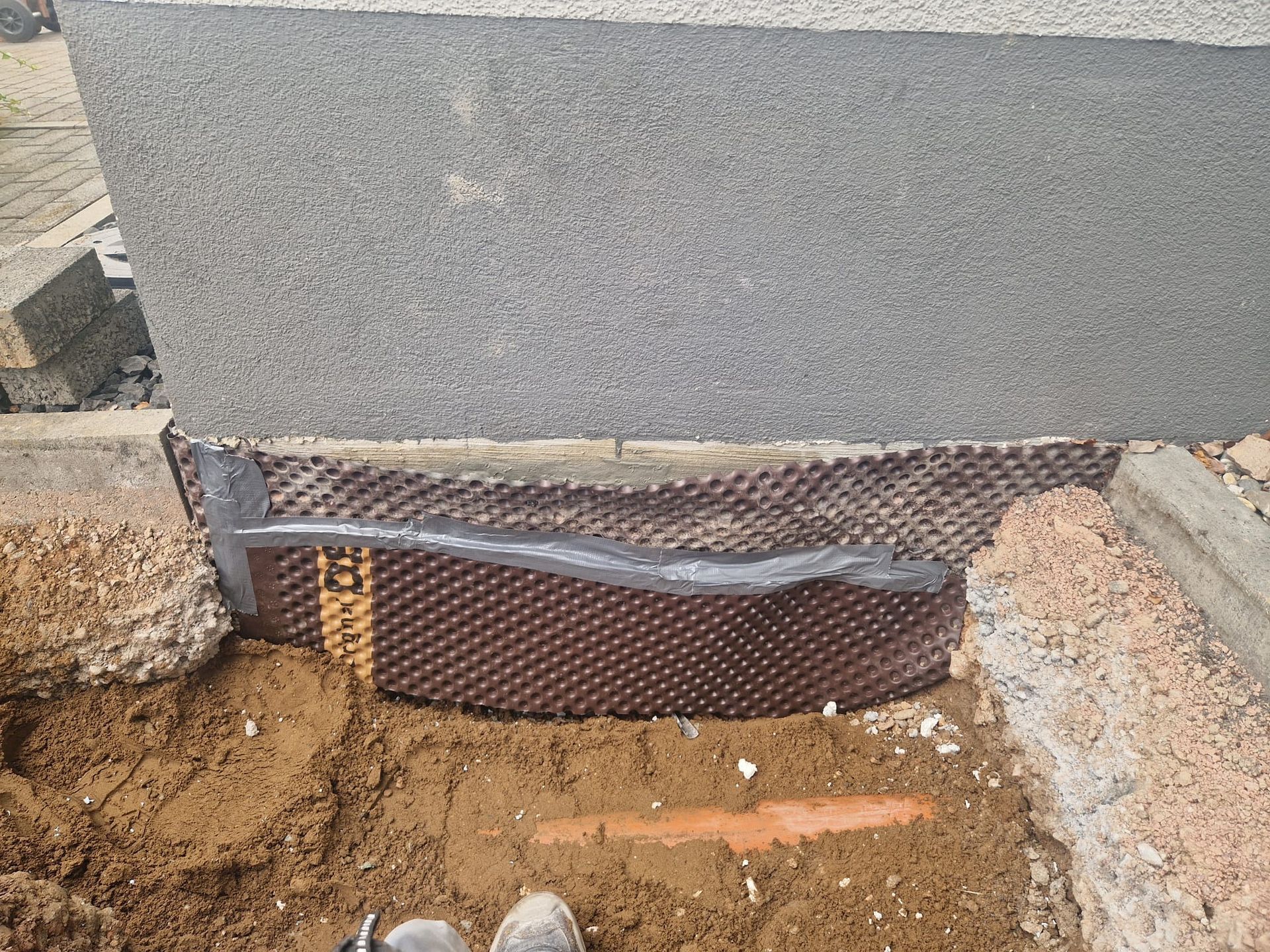 Eine Person steht im Dreck neben einer Betonmauer.