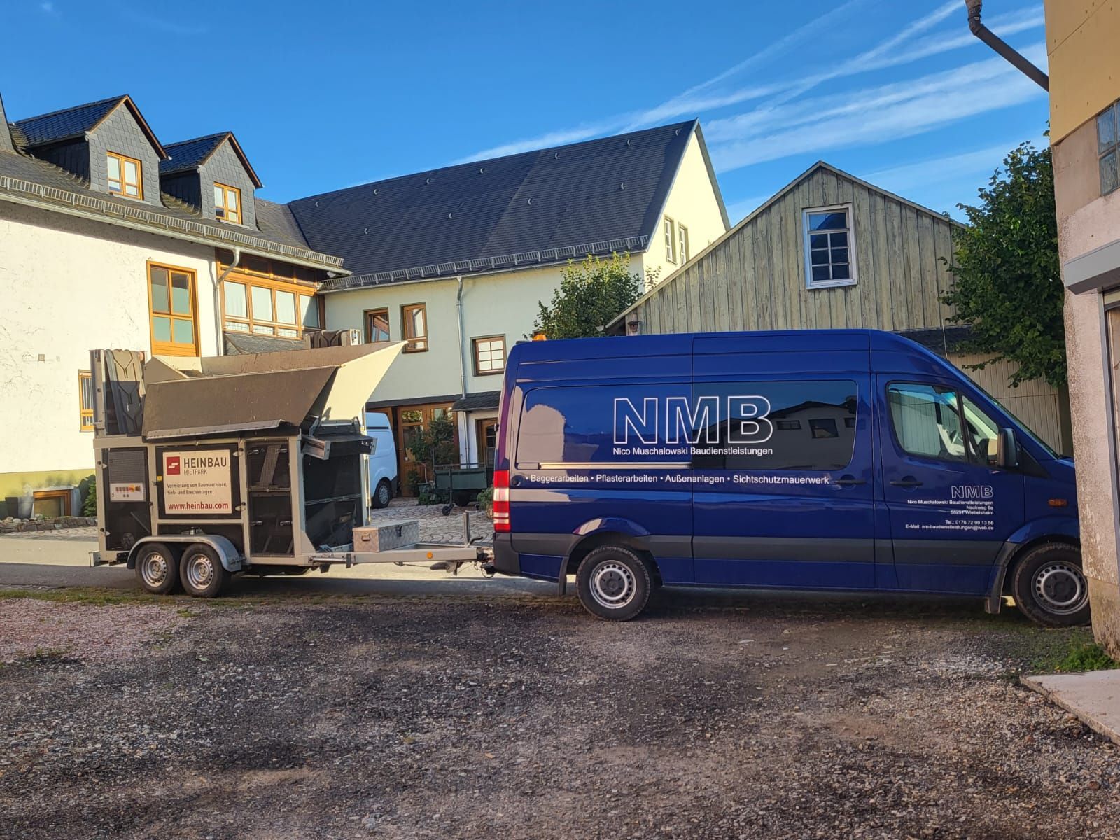 Ein blauer Lieferwagen mit dem Wort NMB an der Seite ist neben einem Anhänger geparkt.