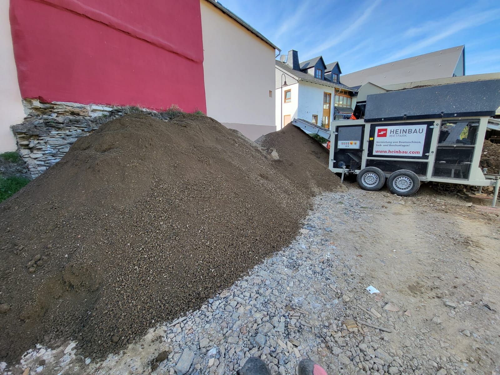 Neben einem Anhänger liegt ein Erdhaufen.