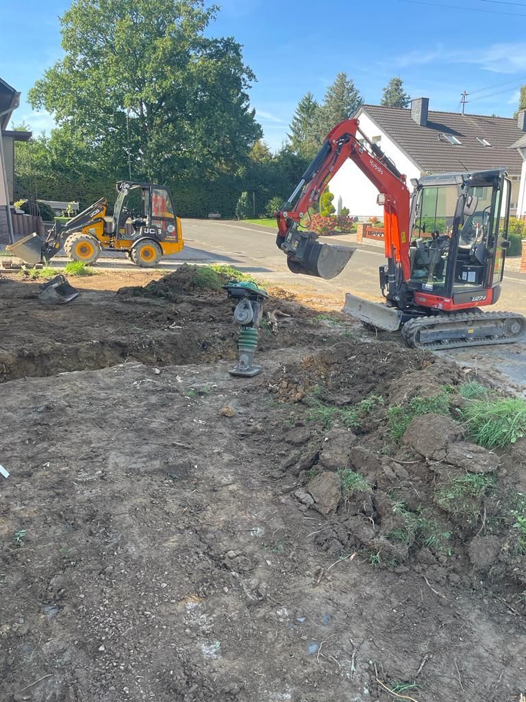 Ein rot-schwarzer Bagger gräbt ein Loch in ein Erdfeld.