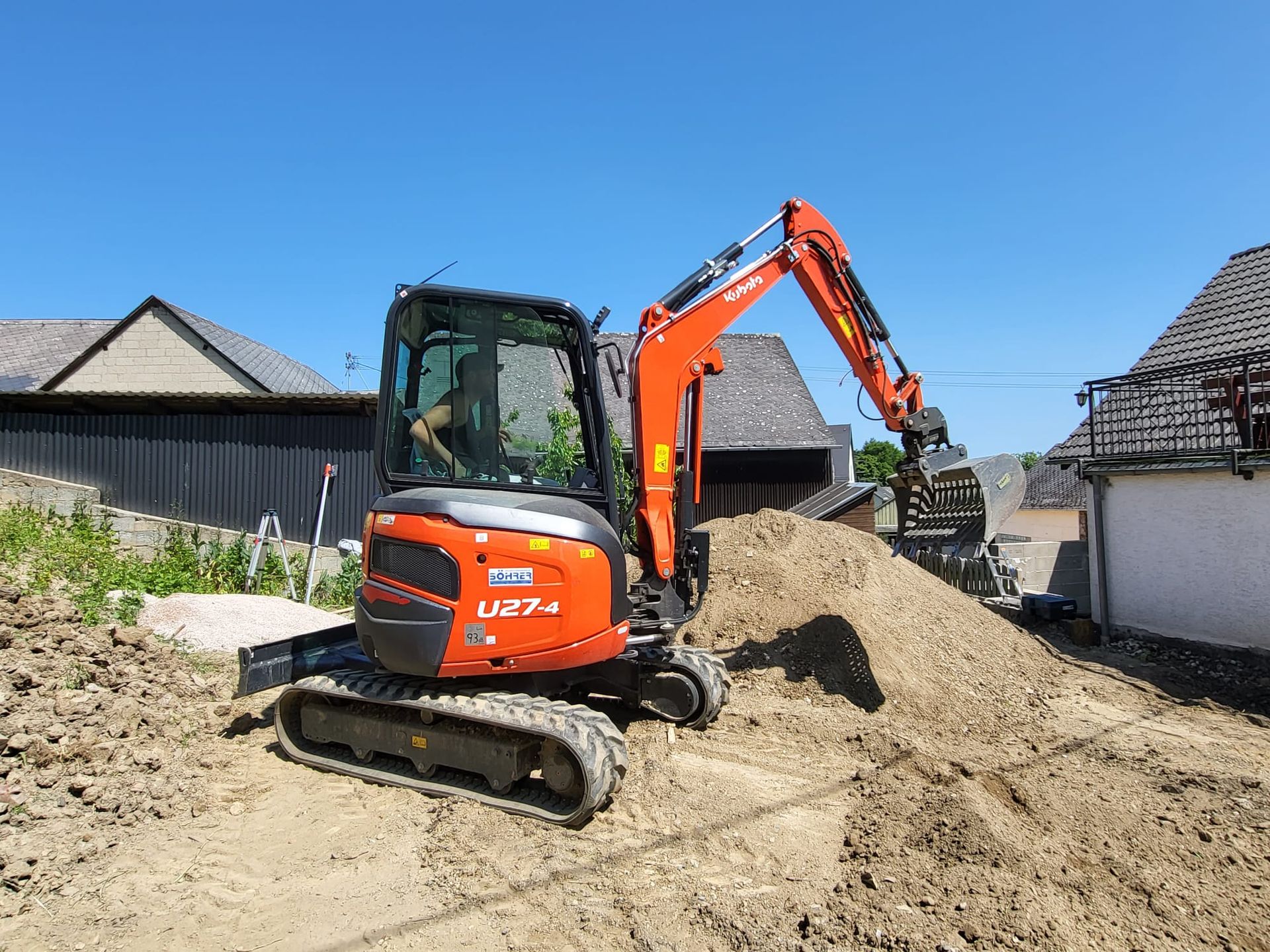 Ein kleiner Bagger gräbt vor einem Haus einen Erdhaufen aus.