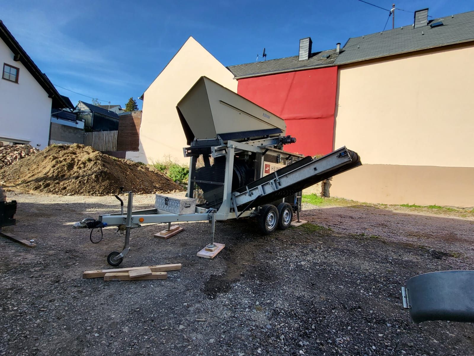 Vor einem Gebäude steht ein Anhänger mit einem daran befestigten Förderband.