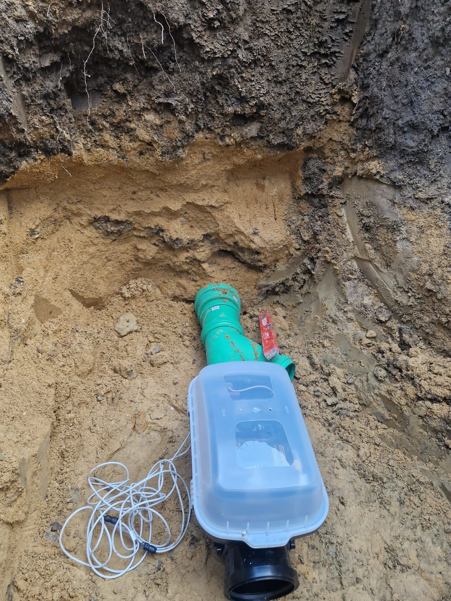 Ein grünes Rohr liegt im Dreck neben einem Plastikbehälter.