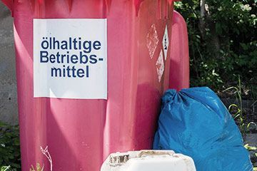 Eine rote Mülltonne mit einem Schild darauf, auf dem steht „ölhaltige Betriebsmittel“.
