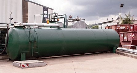 Vor einem Gebäude steht ein großer grüner Tank mit einer daran befestigten Leiter.