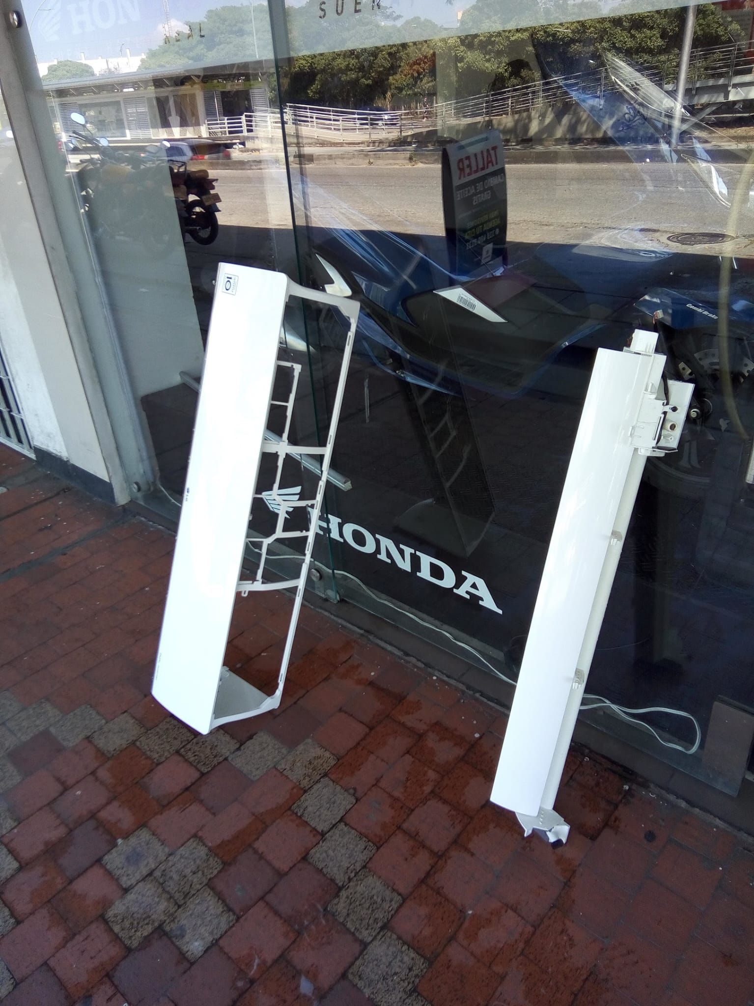 Un aparcabicicletas blanco apoyado contra el escaparate de cristal de una tienda con un letrero de Honda y reflejos de la calle.