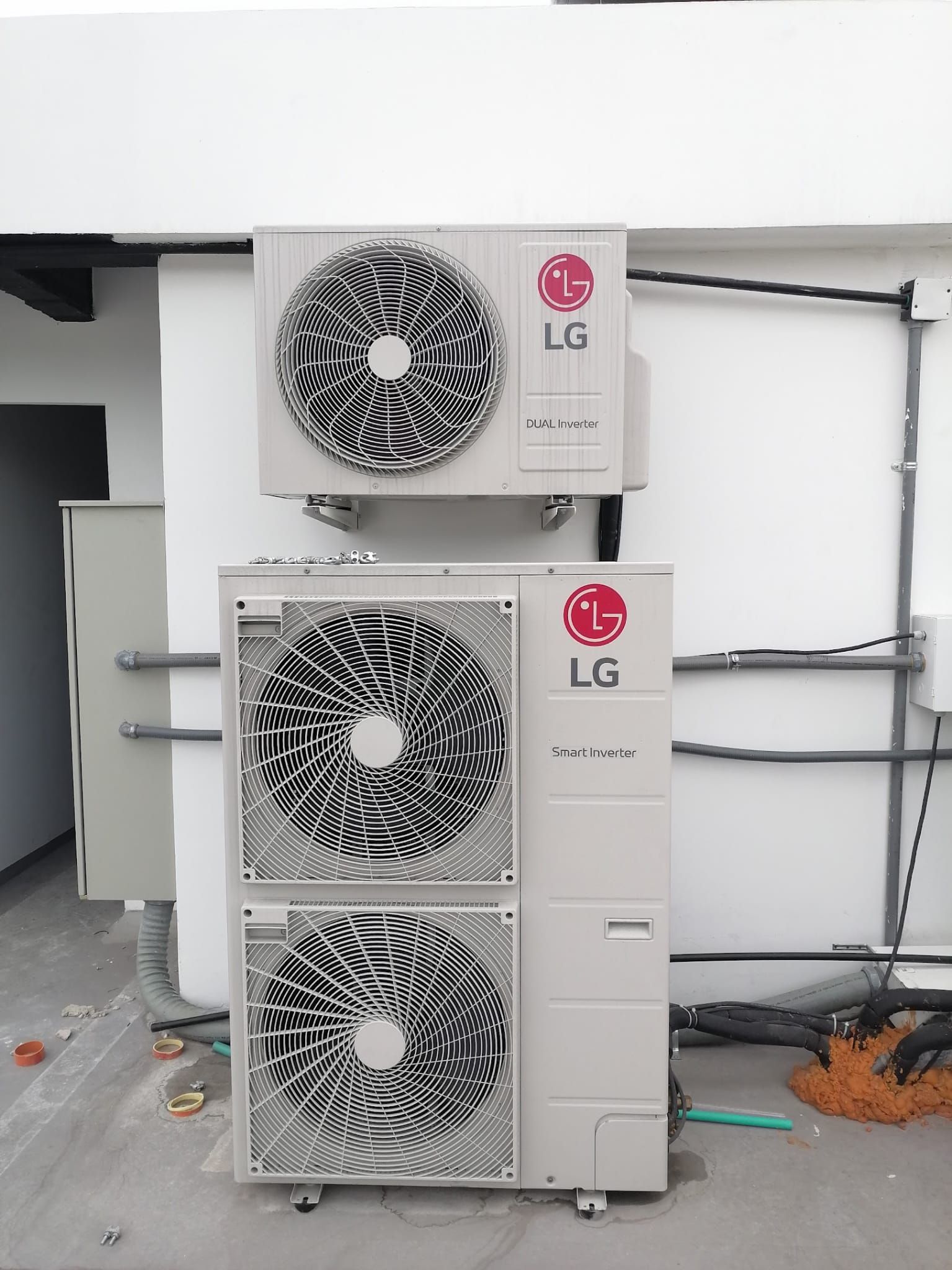 Tres unidades condensadoras exteriores de aire acondicionado LG apiladas contra una pared, con escombros en el suelo y tuberías visibles.
