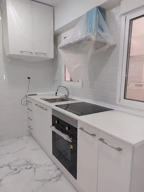 Una cocina con gabinetes blancos, una estufa, un fregadero y una ventana.