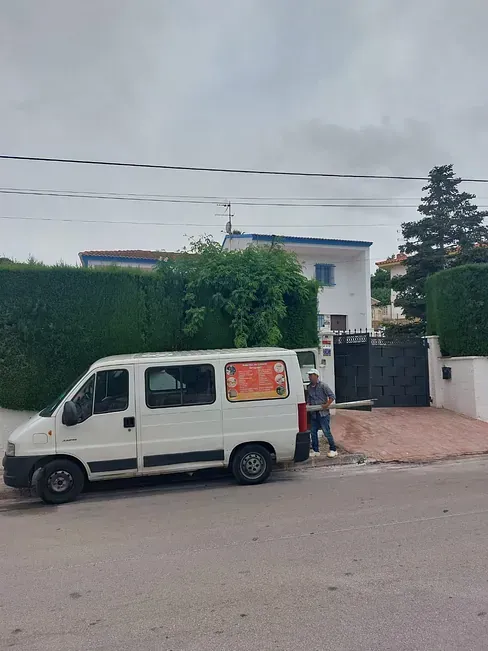 Una camioneta blanca está estacionada al costado de la carretera frente a una casa.