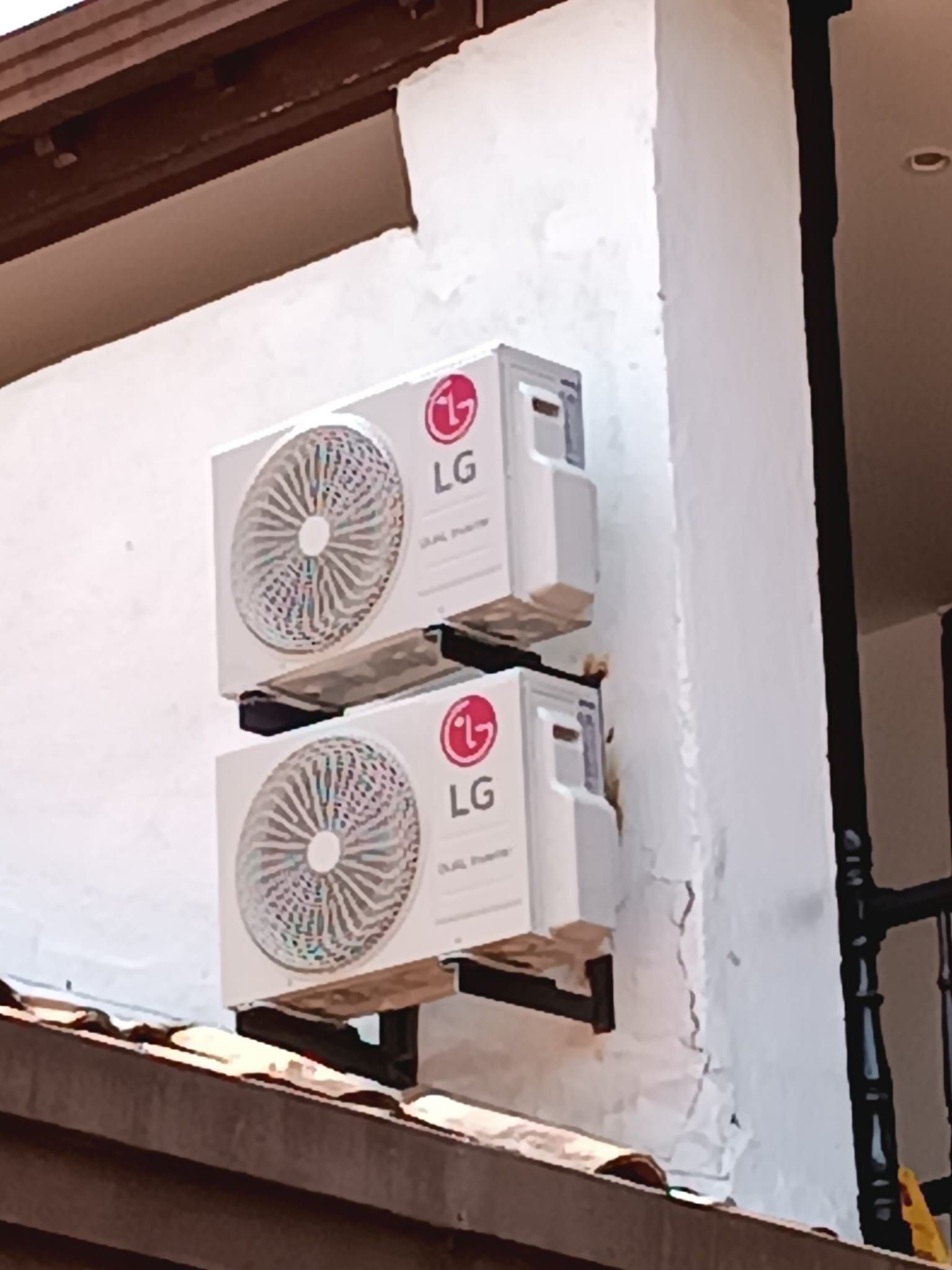 Dos unidades exteriores de aire acondicionado LG blancas montadas en la pared de un edificio cerca del tejado y una ventana.