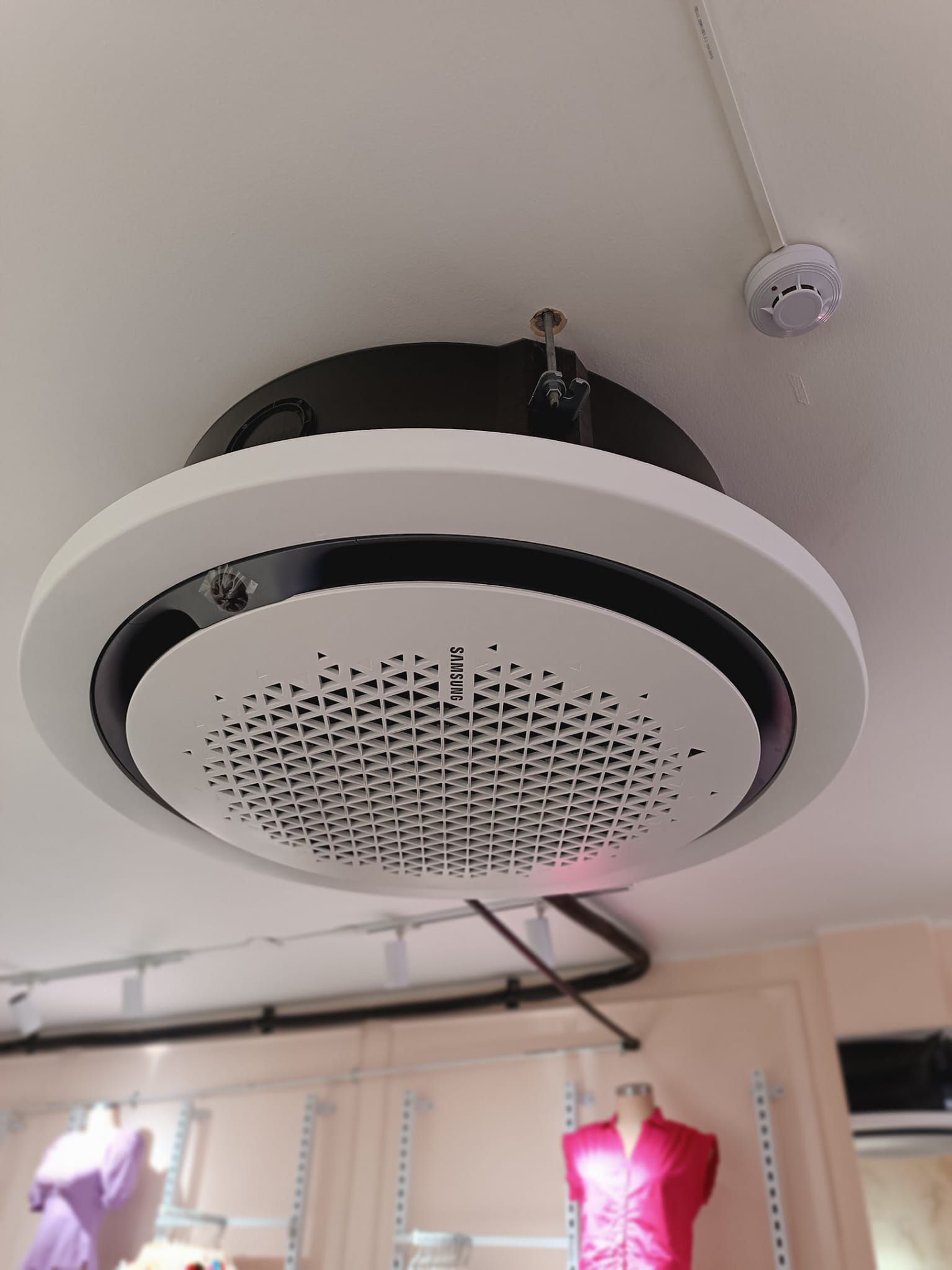 Altavoz redondo o rejilla de ventilación montado en el techo con carcasa blanca y negra en el techo de una tienda.