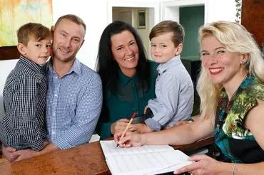 Eine Familie sitzt an einem Tisch und eine Frau unterschreibt ein Dokument.